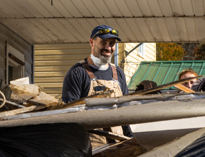 a person in overalls and sunglasses standing in front of a pile of debris