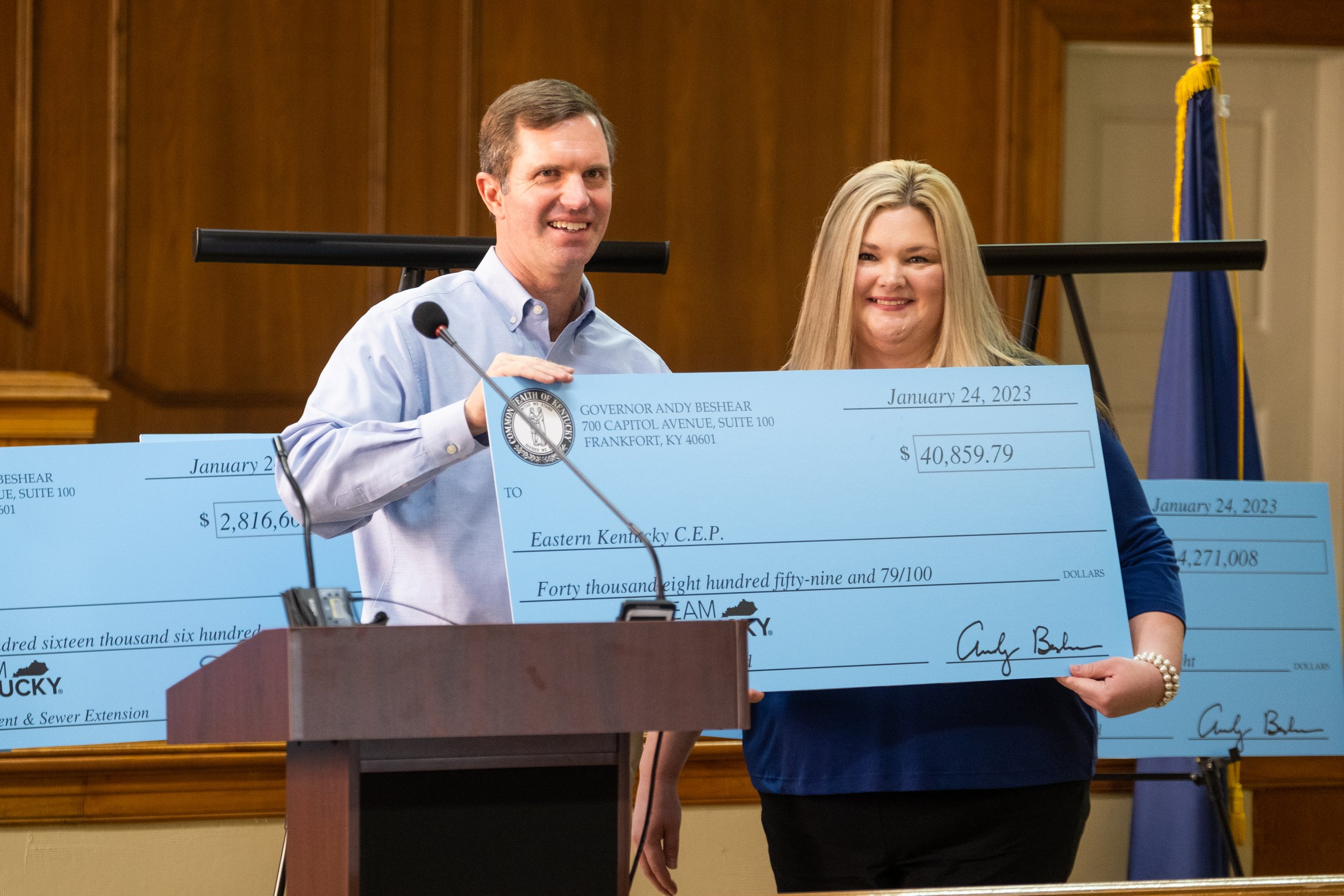 a person and person standing at a podium holding a large check
